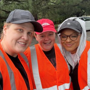 Three members of the Marit Digital team pose together for a selfie wearing baseball hats and orange safety vests.